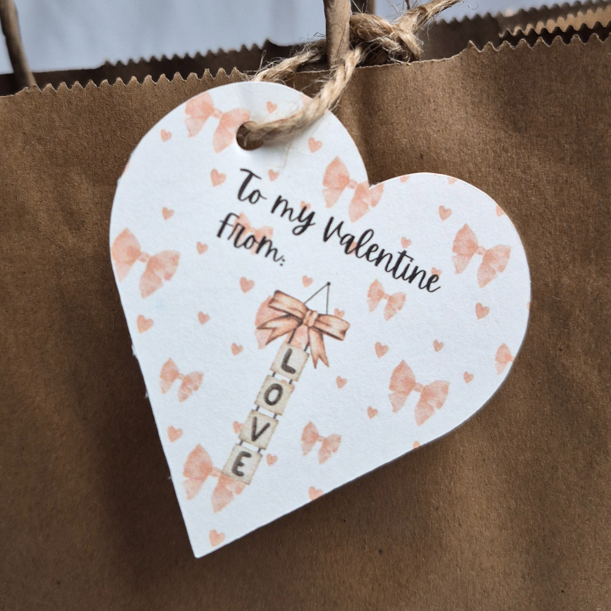 Heart shaped recycled paper Gift tag Valentine's day themed, with pink bows in the background and 'To my Valentine' text. and 'LOVE' hanging vertically.