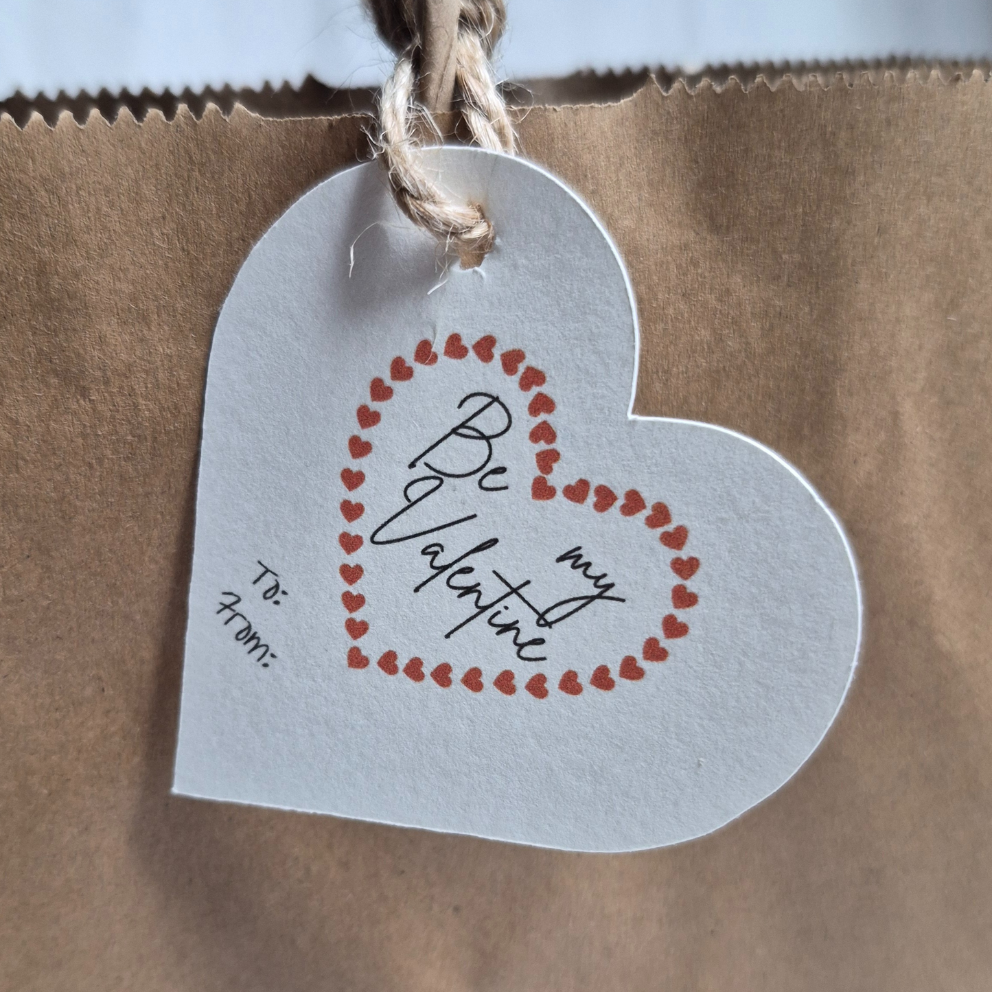 Heart-shaped Eco-friendly gift tag with 'Be my Valentine' text. Hanging from a brown paper bag