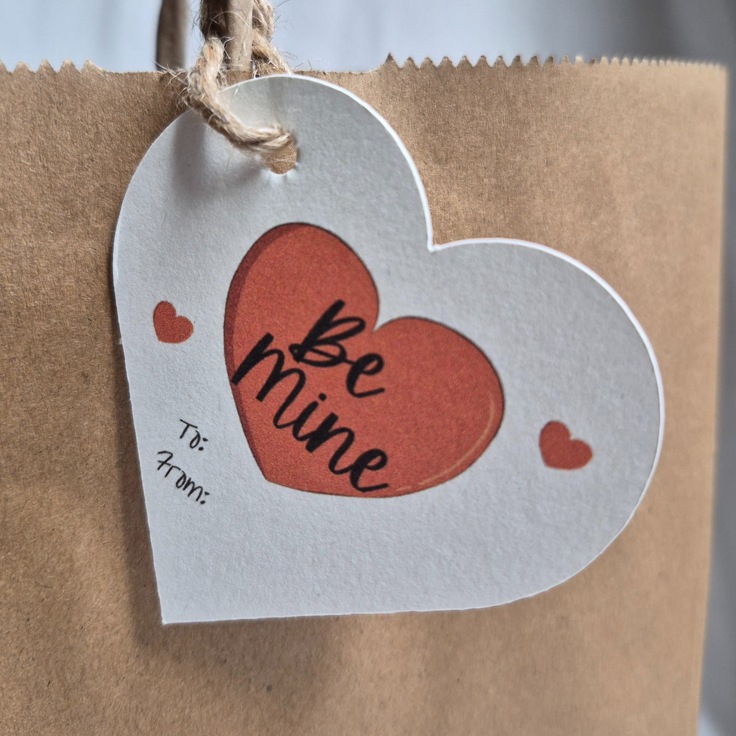 Valentine's day  heart-shaped recycled paper gift tag with 'Be mine' text.  Hanging from a  black bag