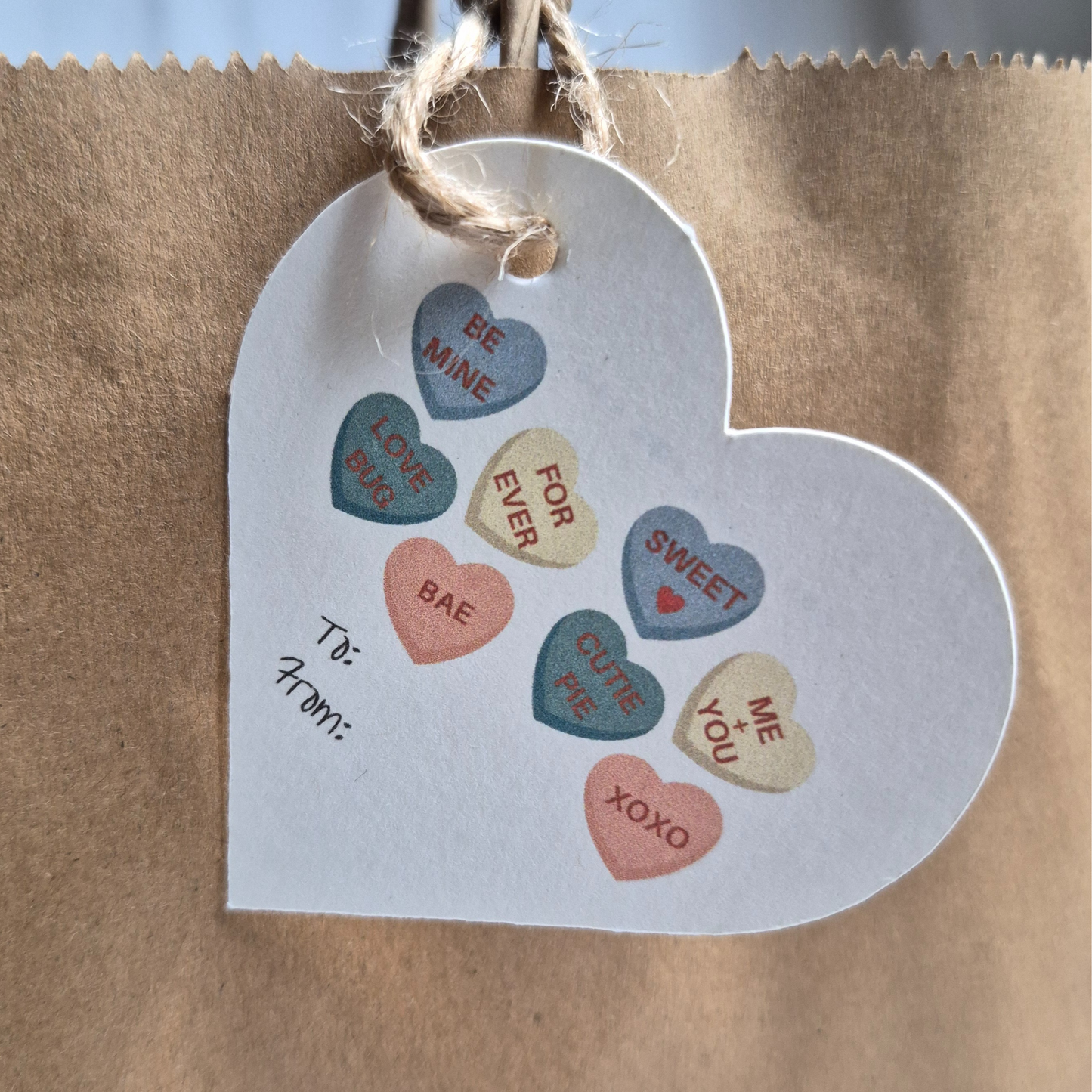 Heart-shaped  recycled paper gift tag with candy heart designs on a brown paper bag.